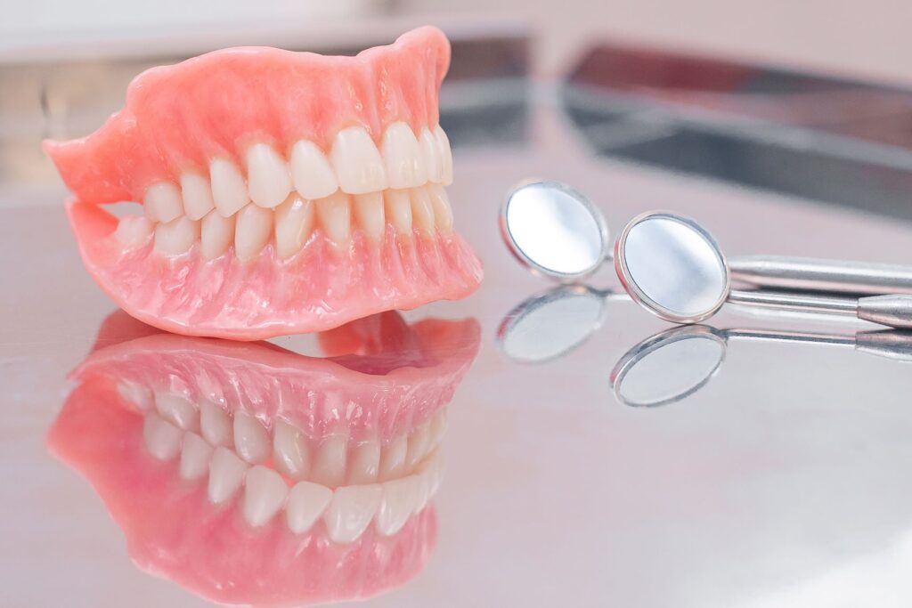 Full set of dentures on a reflective metal tray next to dental mirror